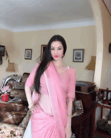 a woman in a pink saree stands in a living room with pictures on the wall