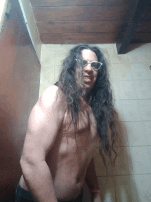 a shirtless man with long hair and glasses stands in a bathroom