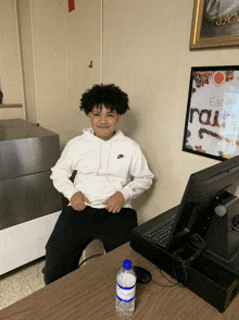 a boy in a white nike hoodie sits at a desk