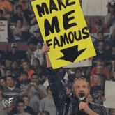 a man holds up a yellow sign that says make me famous
