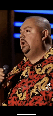 a bald man with a beard is singing into a microphone while wearing a red shirt with dragons on it .