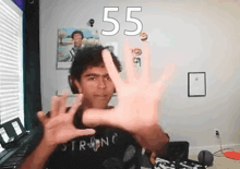 a man wearing a shirt that says strong holds up his hand in front of a wall with the number 55 on it