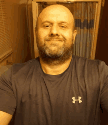 a bald man with a beard wears a grey under armour shirt