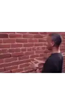 a man in a black shirt is standing in front of a brick wall with his arms crossed .
