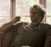 a man is sitting on a couch in front of a window holding a glass of water .