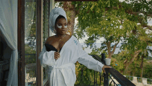 a woman with a towel wrapped around her head is standing on a balcony wearing a bathrobe with the letter h on it