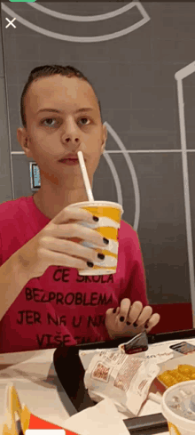 a person wearing a pink shirt that says " ce skola bezproblema " drinking through a straw