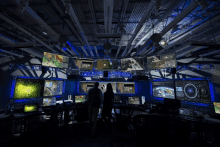 a man and a woman are standing in a room with many monitors