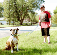 a boy in a red shirt with a spider man shirt on stands next to a dog on a leash