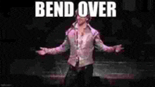 a man in a pink shirt is standing on a stage with his arms outstretched and the words bend over written on the screen .