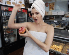 a woman with a towel wrapped around her head is holding a donut in front of a coca cola refrigerator