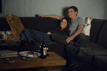 a man and woman sit on a couch with a bottle of wine on the table