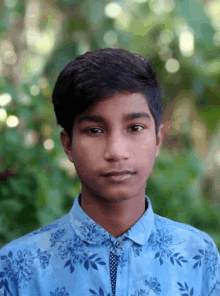 a young man wearing a blue shirt with flowers on it looks at the camera