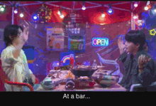 a man and a woman are sitting at a table with an open sign behind them