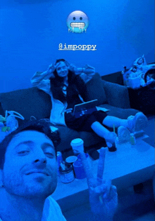 a man giving a peace sign next to a woman sitting on a couch with a blue background that says @impoppy