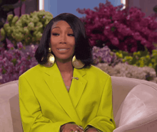 a woman in a bright yellow jacket and gold earrings sits in a chair