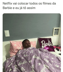 a man is laying in bed with a purple blanket that says barbie on it