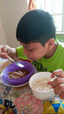 a boy wearing a green shirt that says run is eating from a bowl