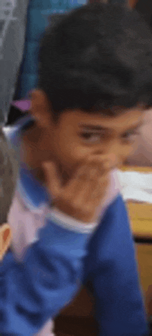 a young boy is sitting at a desk in a classroom with his hand on his face .