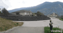 a woman stands on the side of a road looking at a pile of dirt in front of a house