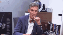 a man in a suit and bow tie is sitting at a desk with a national geographic poster behind him .