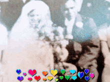 a black and white photo of a man and woman with rainbow colored hearts around them