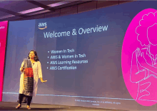 a woman stands in front of a large screen that says welcome & overview