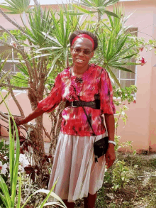 a woman in a red top and white skirt stands next to a palm tree