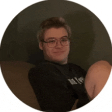 a young man wearing glasses is sitting on a couch and smiling for the camera .