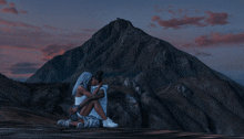 a man and a woman sit on top of a mountain at sunset