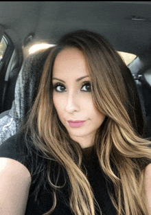 a woman in a black shirt is sitting in a car and taking a selfie