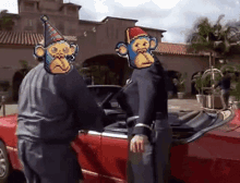 two people with monkey faces on their heads are standing next to a red car