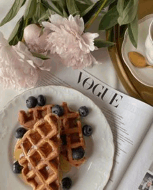 a plate of waffles with blueberries and syrup is sitting on top of a vogue magazine .