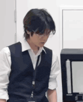 a man wearing glasses and a vest is standing in front of a printer .