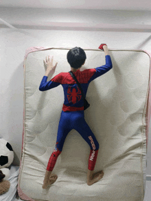 a boy in a spider-man costume is laying on a mattress