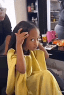 a little girl in a yellow dress is sitting in a chair getting her hair done .