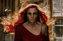 a woman with long red hair is standing in front of a window with fire coming out of her hair
