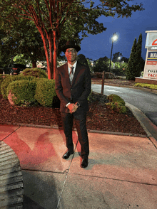 a man in a suit and hat stands on a sidewalk in front of a sign that says ' taco ' on it