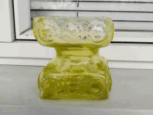 a yellow vase sits on a window sill in front of blinds