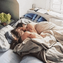 a man and woman are laying in bed under a blanket and kissing