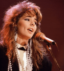 a woman singing into a microphone while wearing pearls