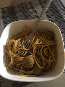 a white bowl of spaghetti and meatballs with a fork in it