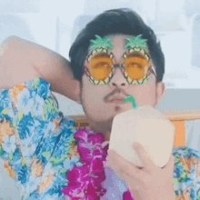 a man wearing pineapple sunglasses is drinking a coconut