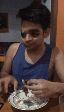 a man in a blue tank top is eating food from a bowl