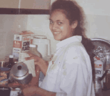 a woman in a kitchen with a box of kellogg 's corn flakes in the background