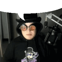 a man wearing a top hat , goggles and a hoodie is standing in front of a microphone .