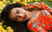 a woman in a red dress is laying on the ground in front of a pile of lemons .