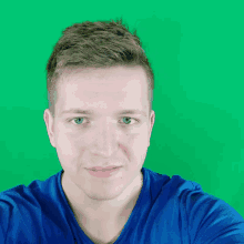 a man in a blue shirt is taking a selfie with a green background