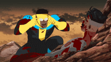 a man in a yellow and blue superhero costume is kneeling next to a man in a bloody suit