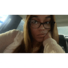 a woman wearing glasses and a sweater is taking a selfie in a car .